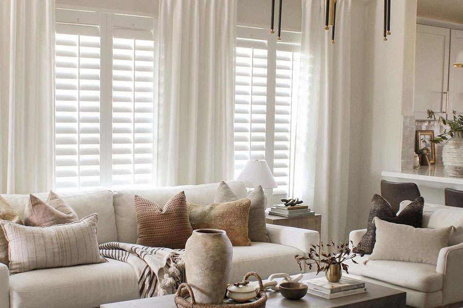Custom interior shutters lend beauty and personality to your home. Photo Credit: @ BrookeMoralesHome Brown and off-white living room with white polywood shutters.